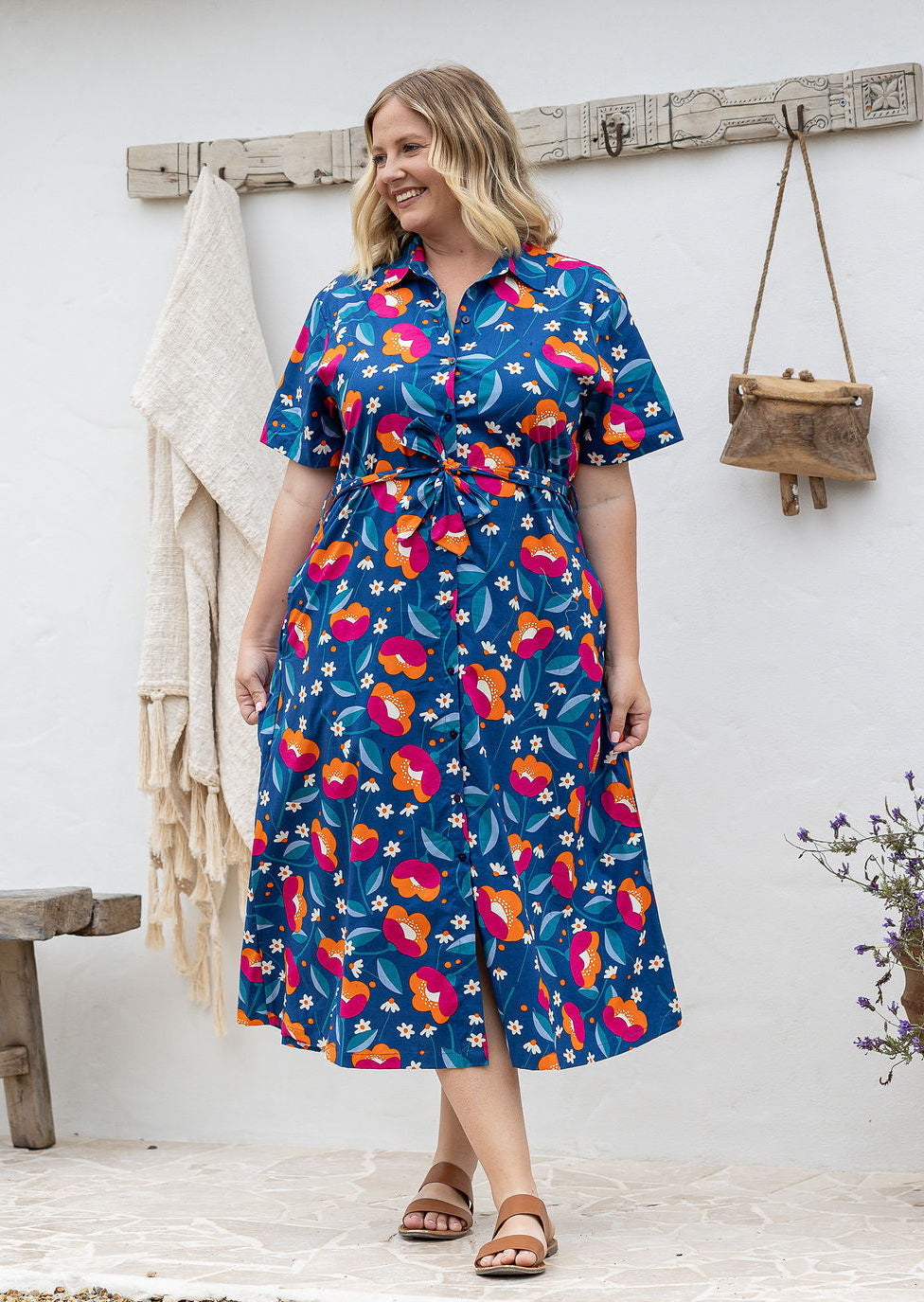 Woman wearing 100 percent cotton button through shirt dress with collar and short sleeves, in a royal blue based floral print.