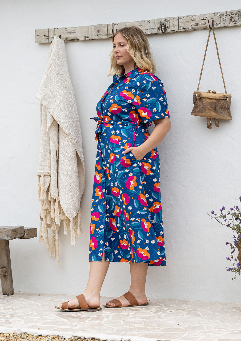 Model standing sideways wearing a floral printed shirt dress with hand in pockets