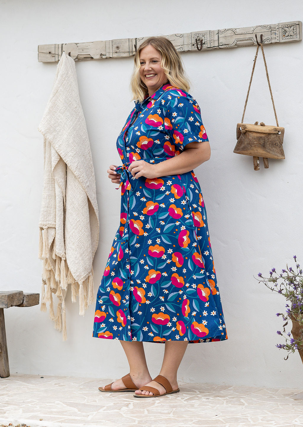 Model stands wearing a shirt style button through cotton dress with collar and a removable waist tie.