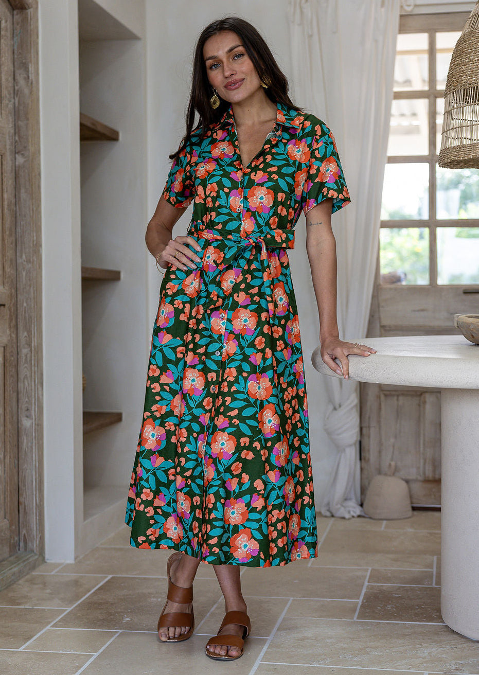 Woman wearing 100 percent cotton button through shirt dress with collar and short sleeves, in a olive green based floral print.