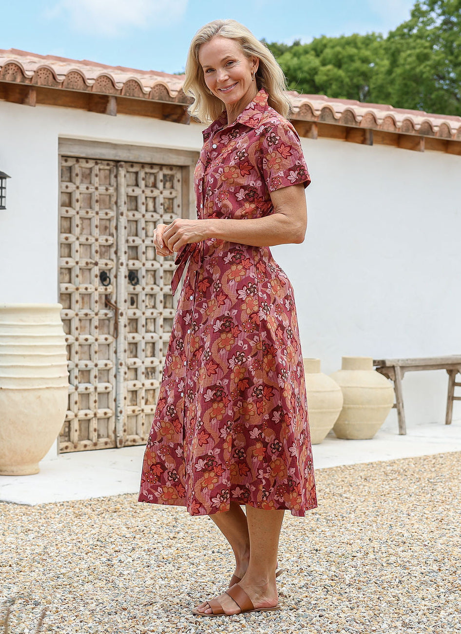 Woman standing sideways wears a retro cotton shirtstyle dress in a Japanese floral print, in front of a rustic wooden door.