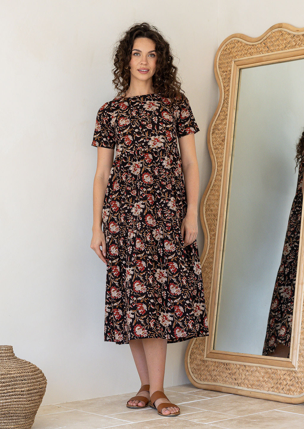 Woman wearing a 100% cotton, midlength black dress featuring three tiered design, short sleeves, high round neckline and pockets