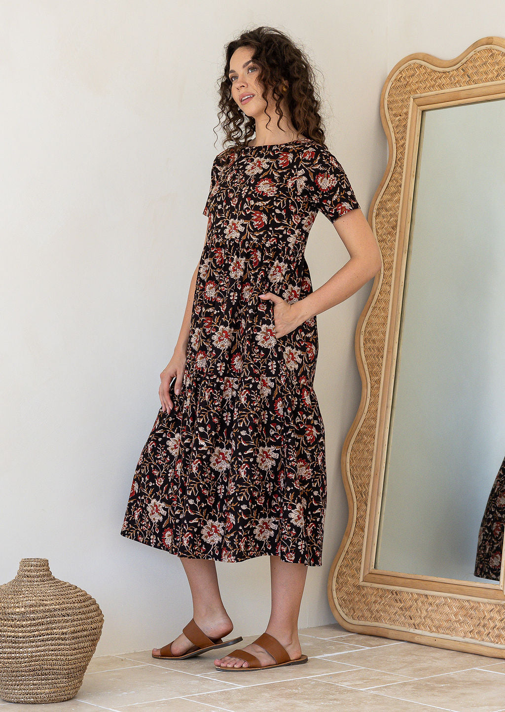 Woman wearing a relaxed fit printed black cotton dress with tiered design, standing next to a large mirror
