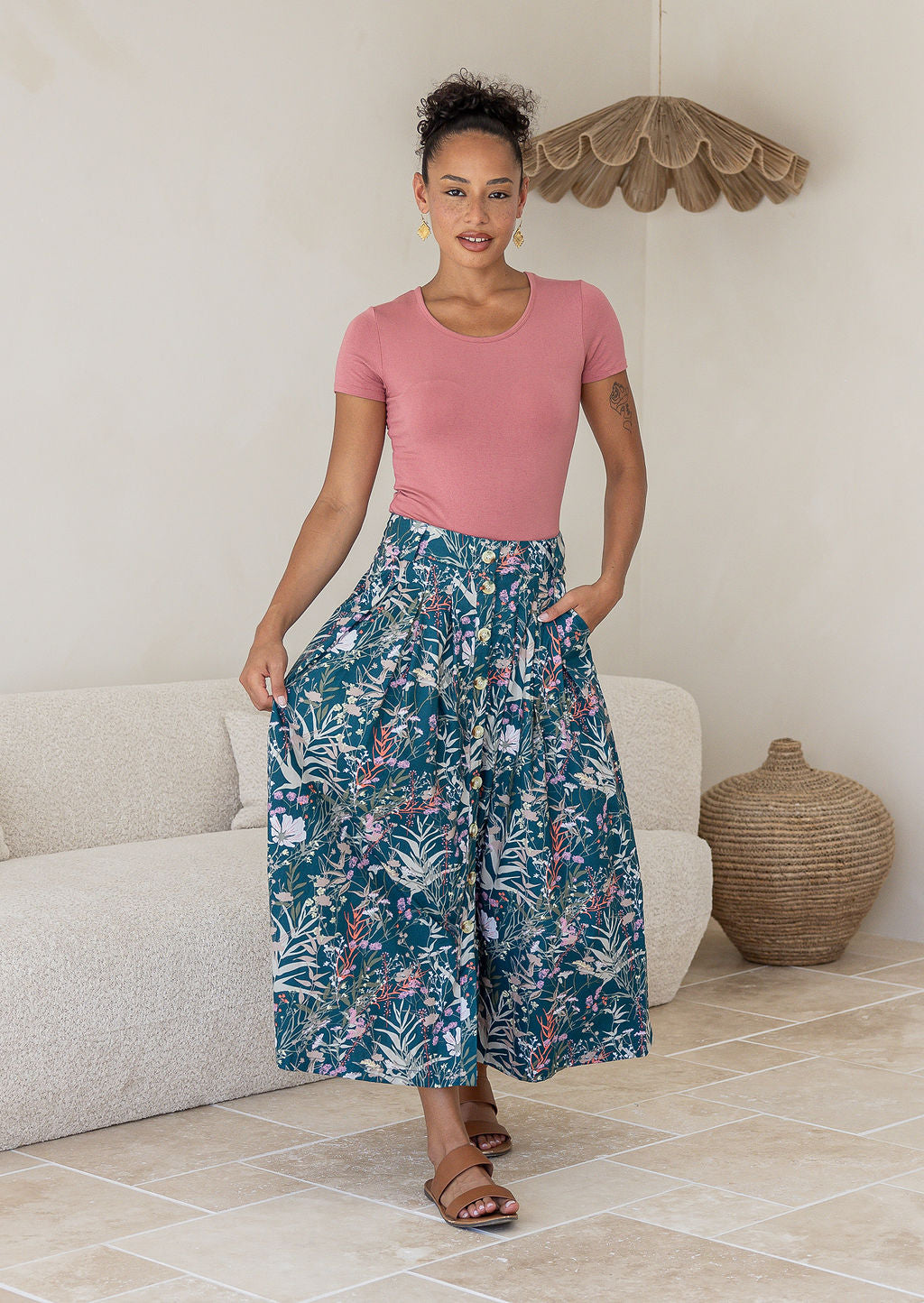 Woman wearing a pink top and green floral cotton floral maxi skirt in a room with with her hand in one pocket