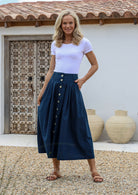 Woman standing with a hand in pocket wearing a 100% cotton shin length, button through, pleated skirt with belt loops