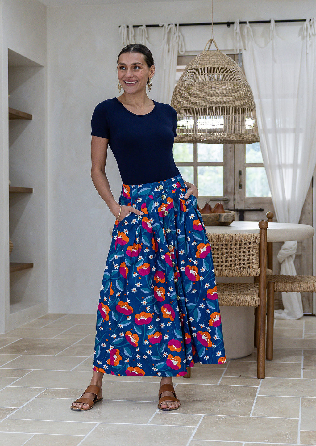 Woman wearing a basic top and floral button through shin length cotton skirt with box pleats, belt loops and pockets.