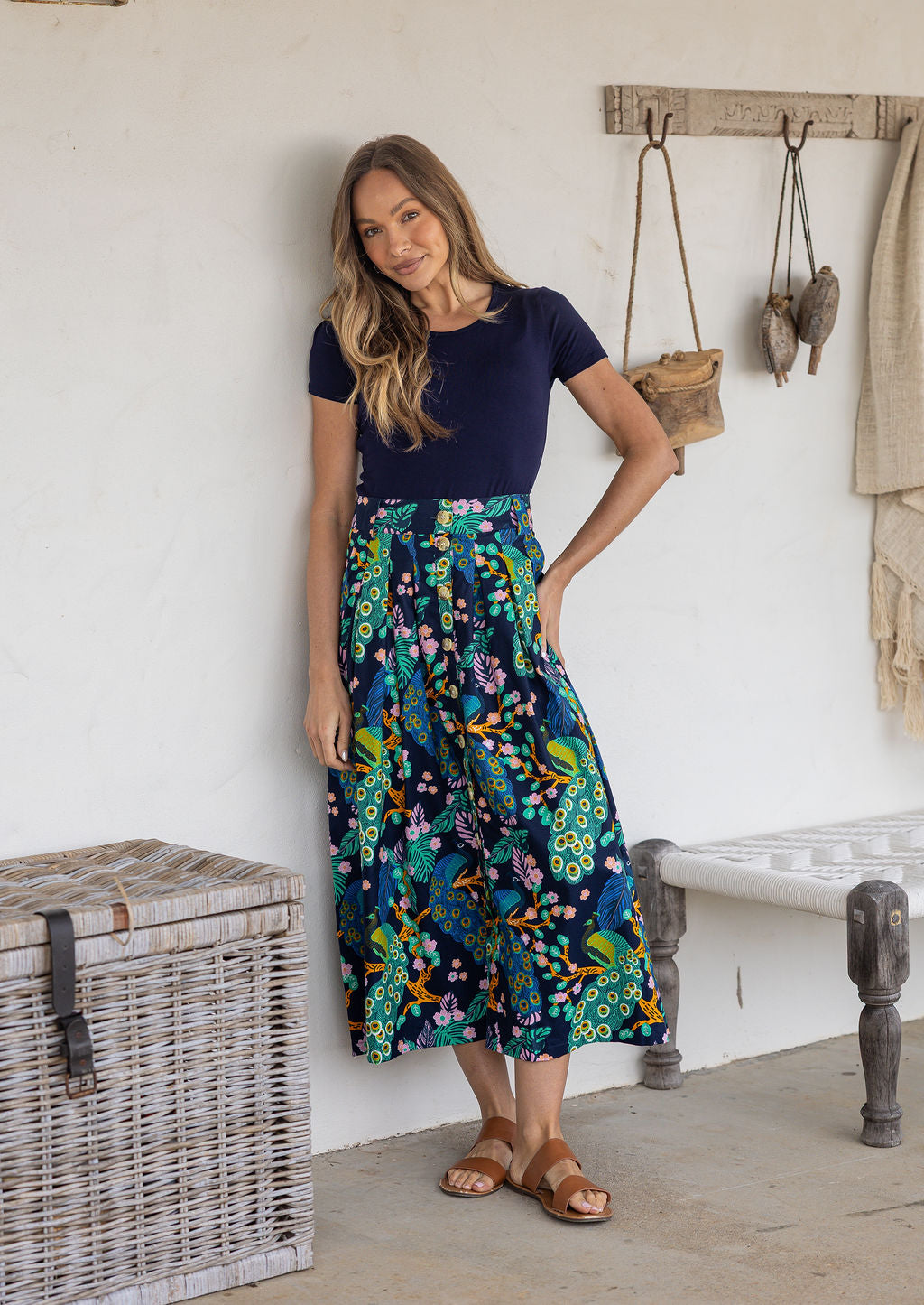 Woman wearing a navy basic top and floral peacock button through shin length cotton skirt with box pleats, belt loops and pockets.