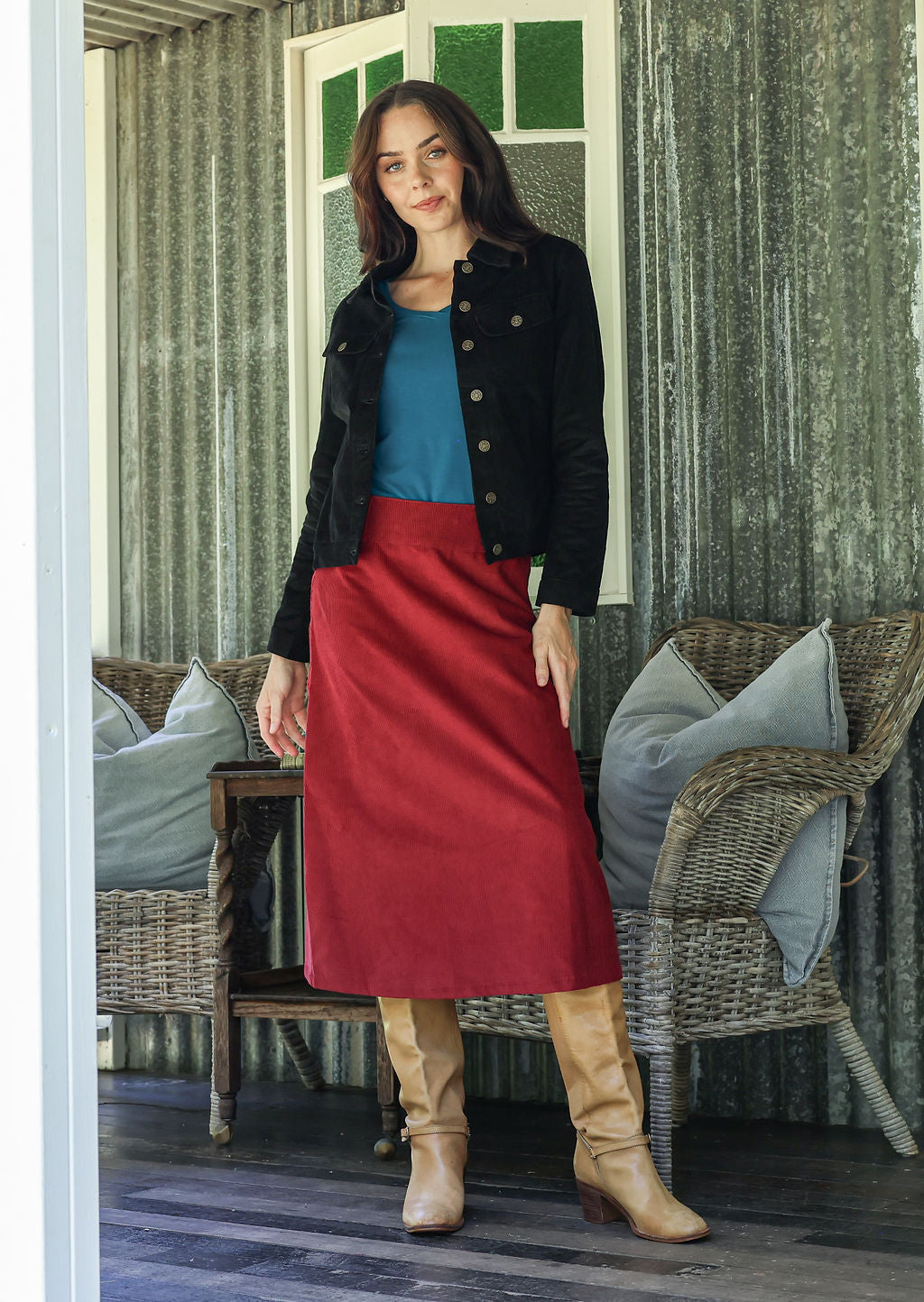 Woman in a red cotton corduroy skirt and black cotton corduroy jacket standing in a room with wicker furniture