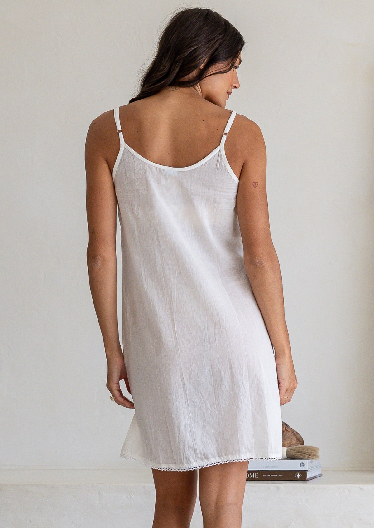 Back view of model wearing white cotton slip undergarment with thin adjustable straps and lace hem, above knee length