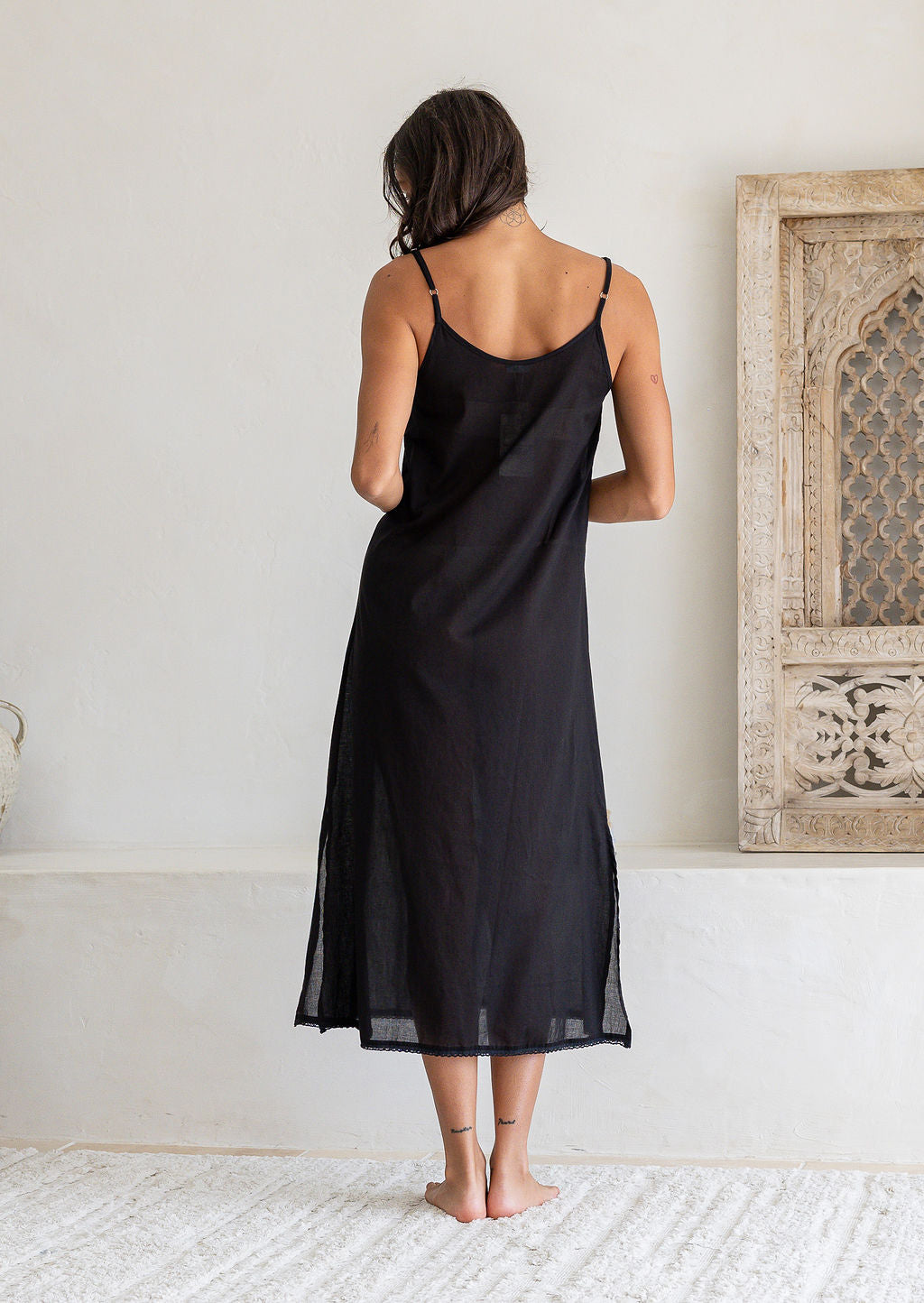 Back view of woman wearing black cotton voile maxi slip with adjustable spaghetti straps and side splits