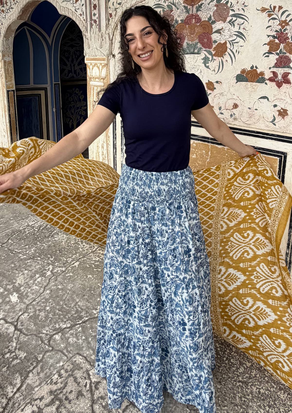 Woman twirls in a white based blue floral cotton maxi skirt paired with a navy blue stretch t-shirt and a yellow shawl