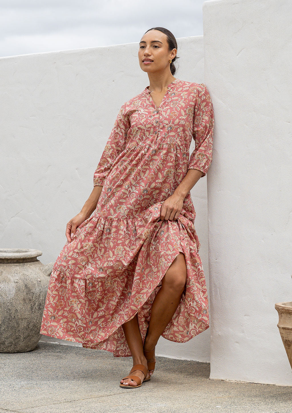 Woman wearing a 100% cotton rose pink based floral dress standing against a white wall.