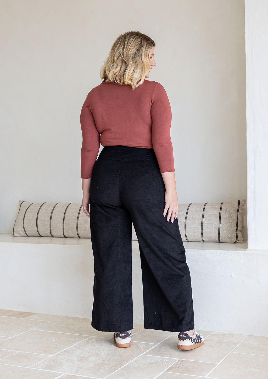 woman standing backwards wearing black corduroy wide leg pants.