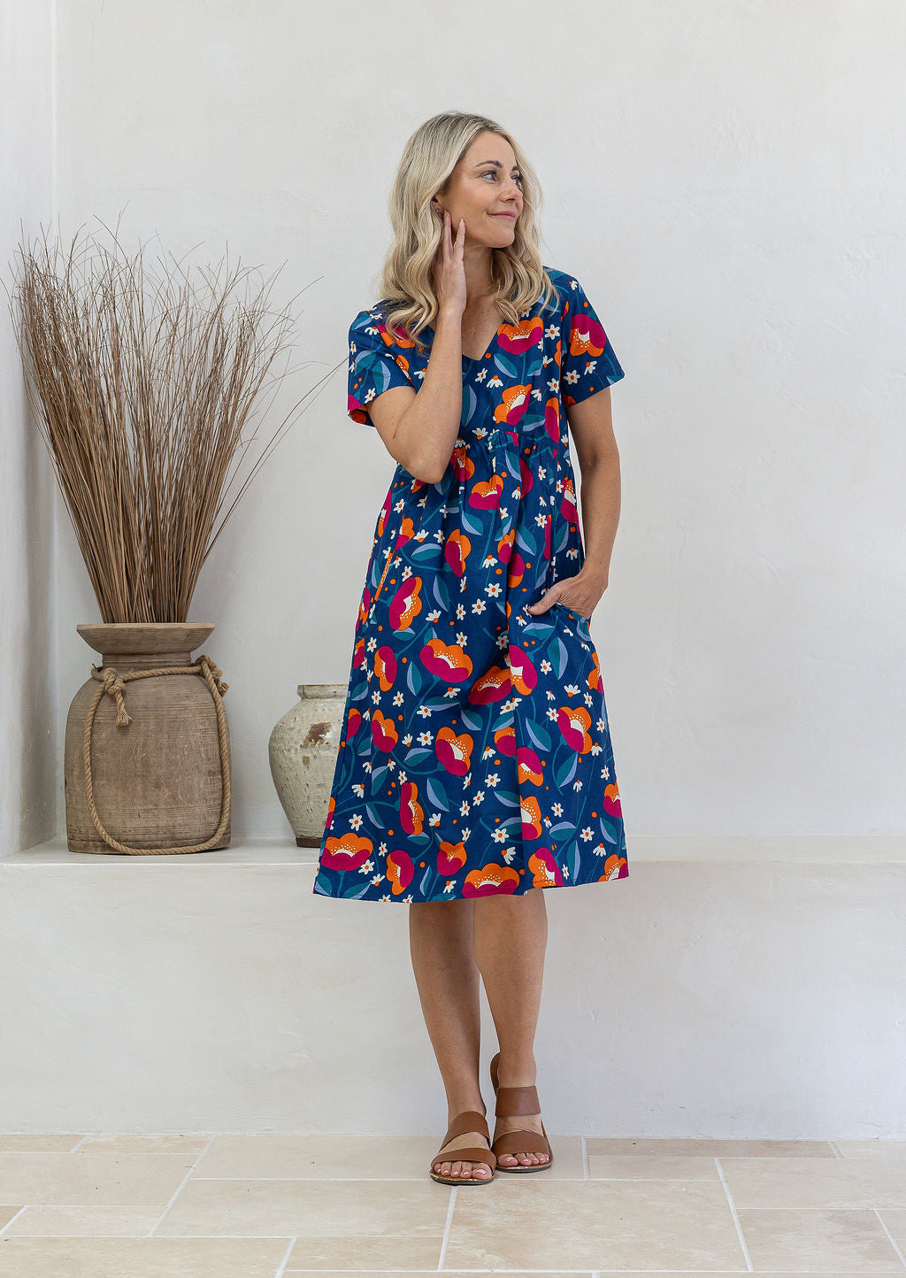 Model wearing a cotton knee length dress with empire waist, short sleeves and one hand in pocket