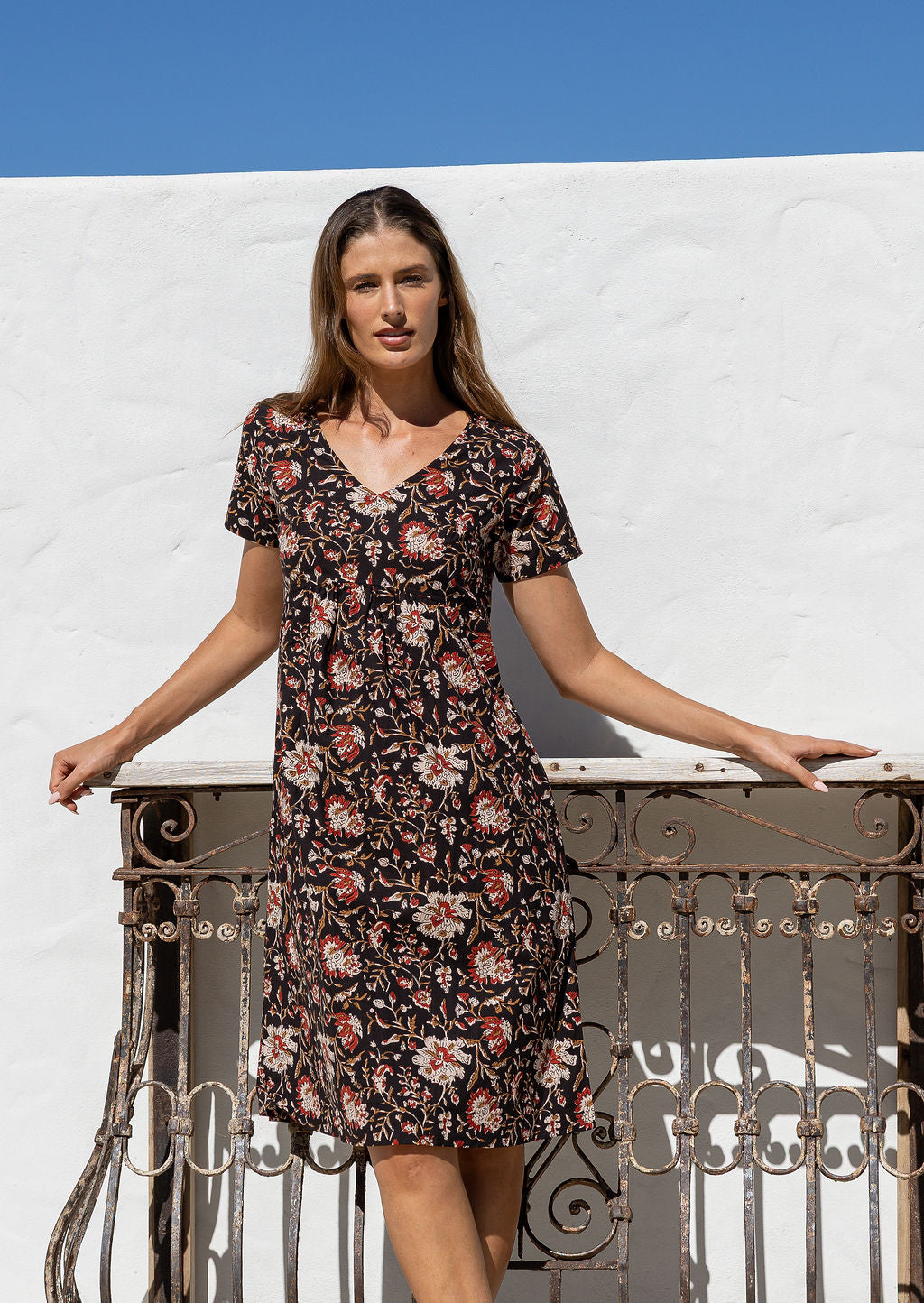 Woman wearing a 100% cotton black based floral print dress with V neckline and short sleeves.
