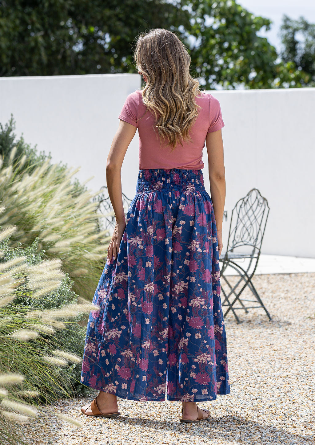 Woman standing backwards wearing a pink top and wide legged navy blue cotton floral pants.