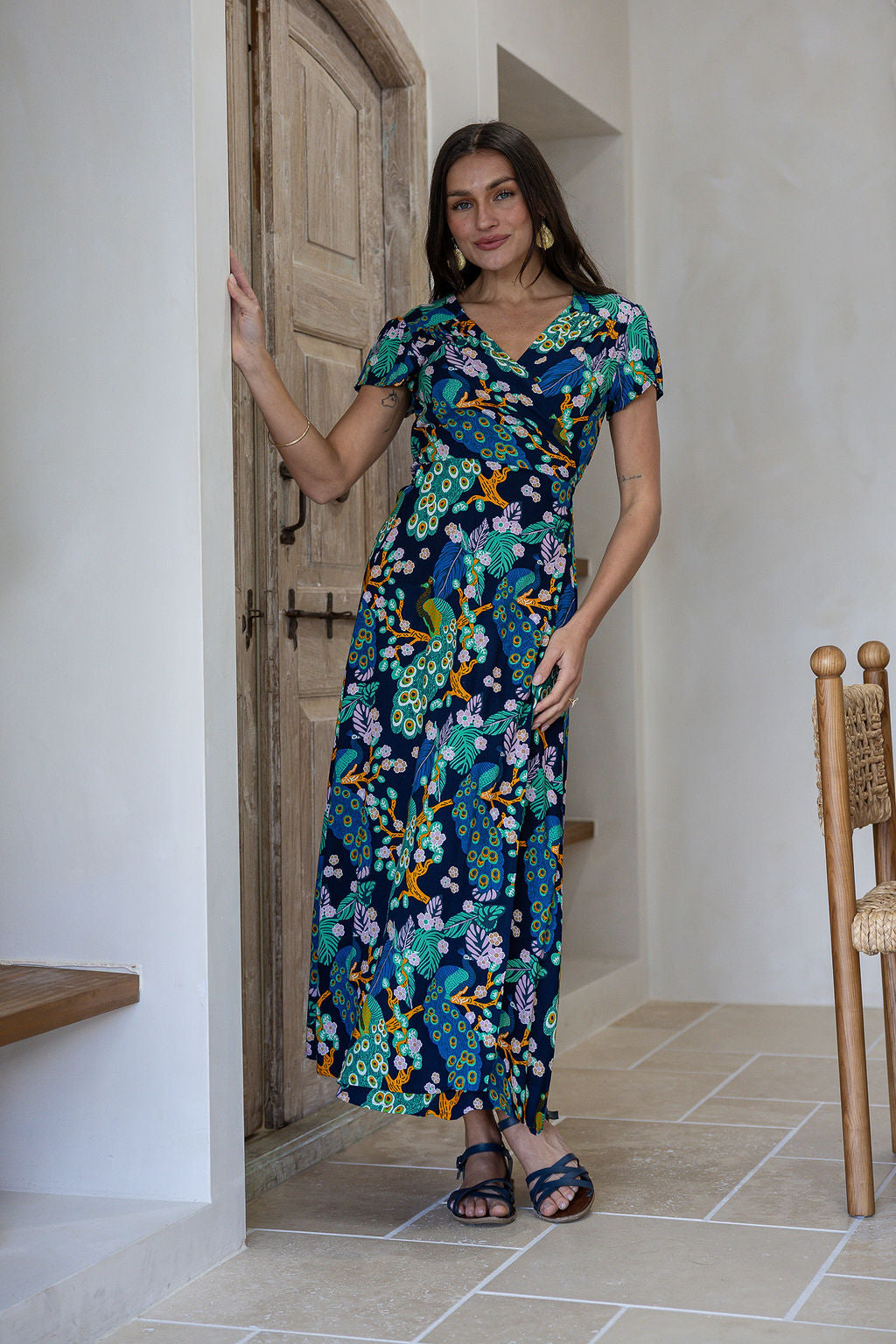 Woman in a navy blue floral rayon wrap dress with butterfly sleeves and small gathers at the shoulder, standing next to a wooden door.