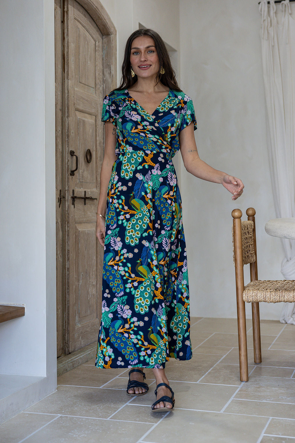 Woman wearing a blue based multicolour floral wrap style maxi rayon dress.