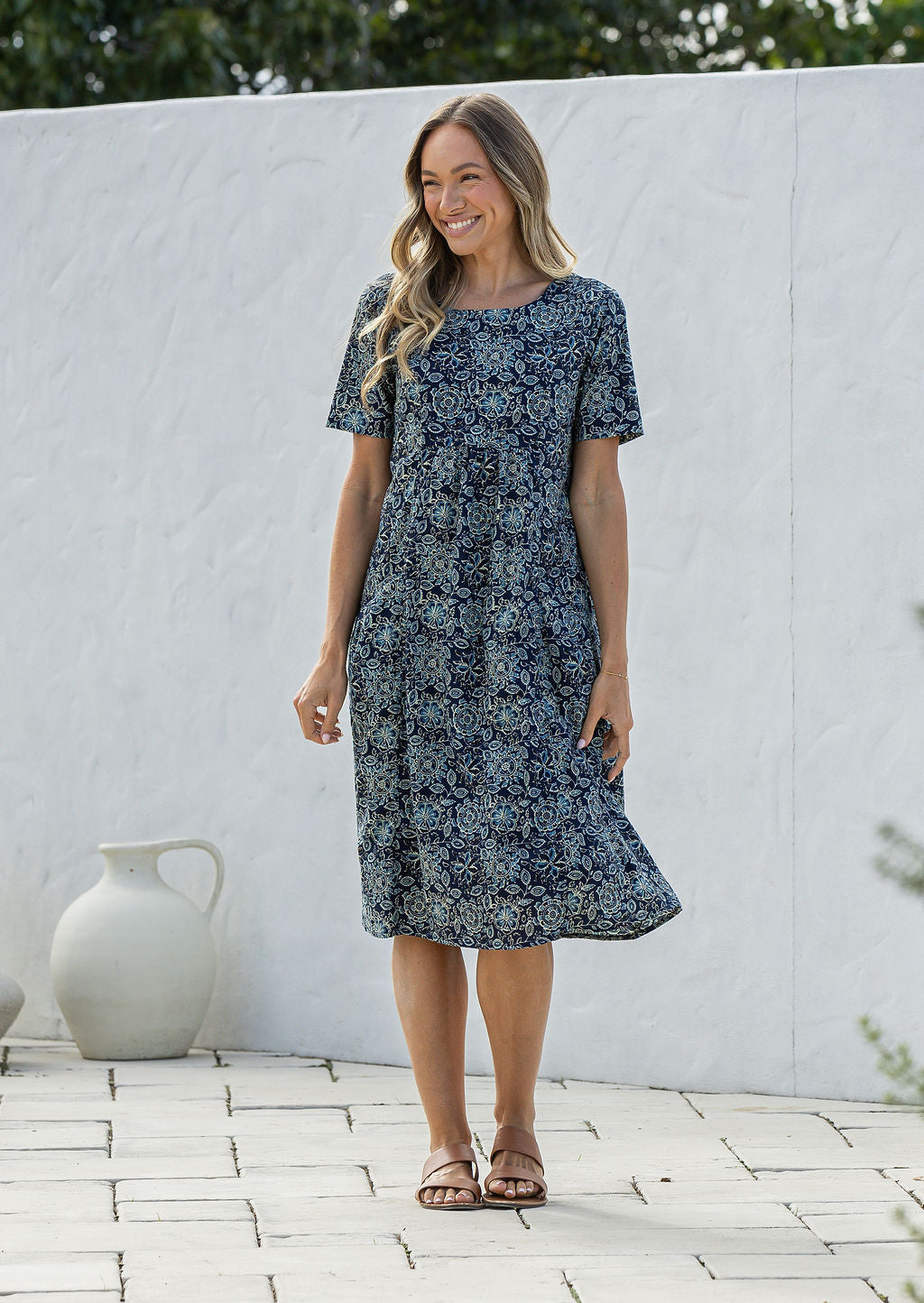 Woman wearing a 100% cotton blue floral dress standing against a white wall.