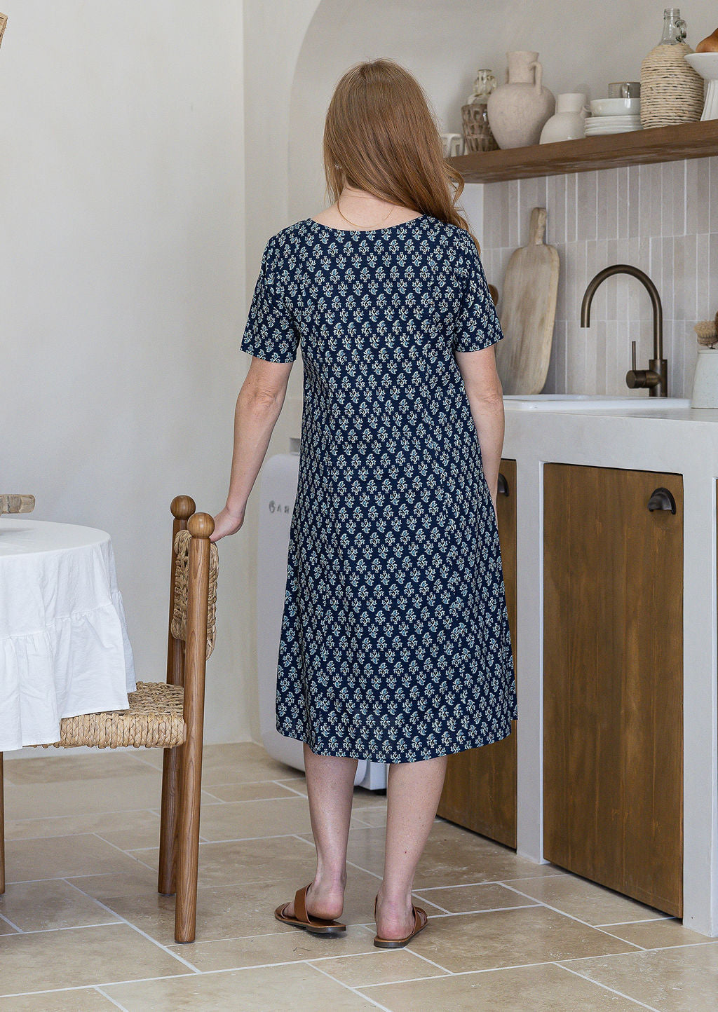 Woman stands backwards wearing a 100% cotton dress in navy blue based floral print with short sleeves