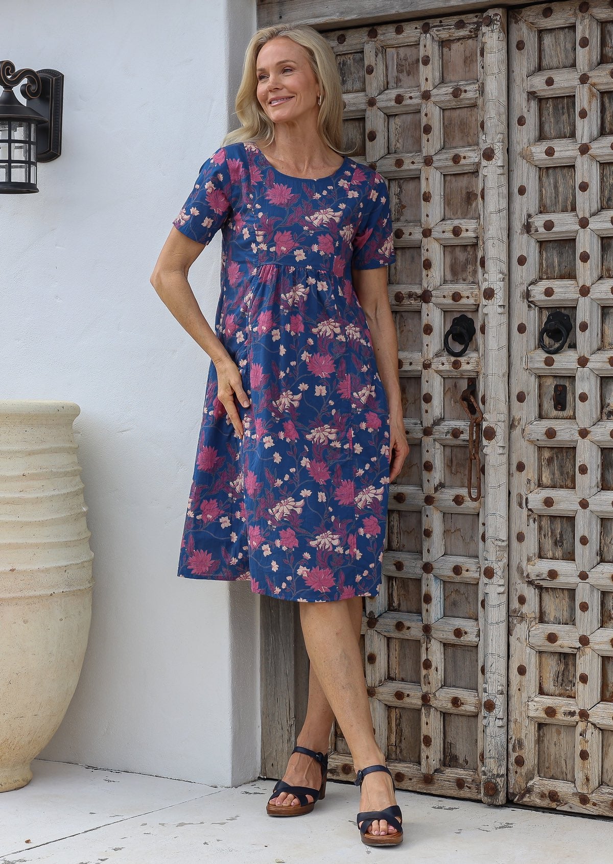 Woman wearing a relaxed fit blue floral cotton dress with round neckline, short sleeves and pockets with pin tucks.