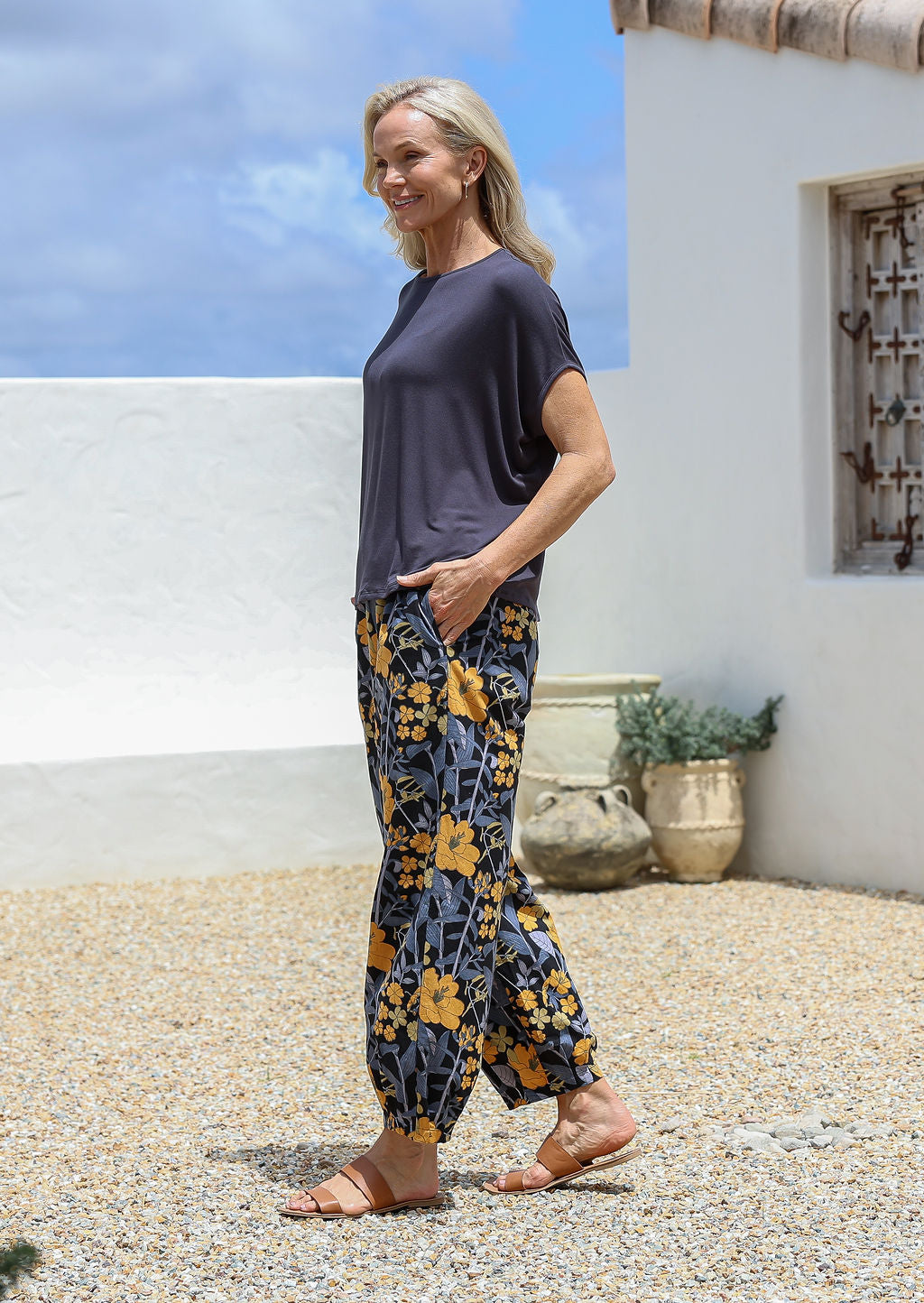 Model stands sideways with one hand in pocket wearing relaxed-fit tapered cotton pants with pleats at the ankles and an elastic waistband.