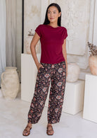 Woman standing in front of white wall with one hand in pockets wears 100% cotton wide leg black pants in nocturne print