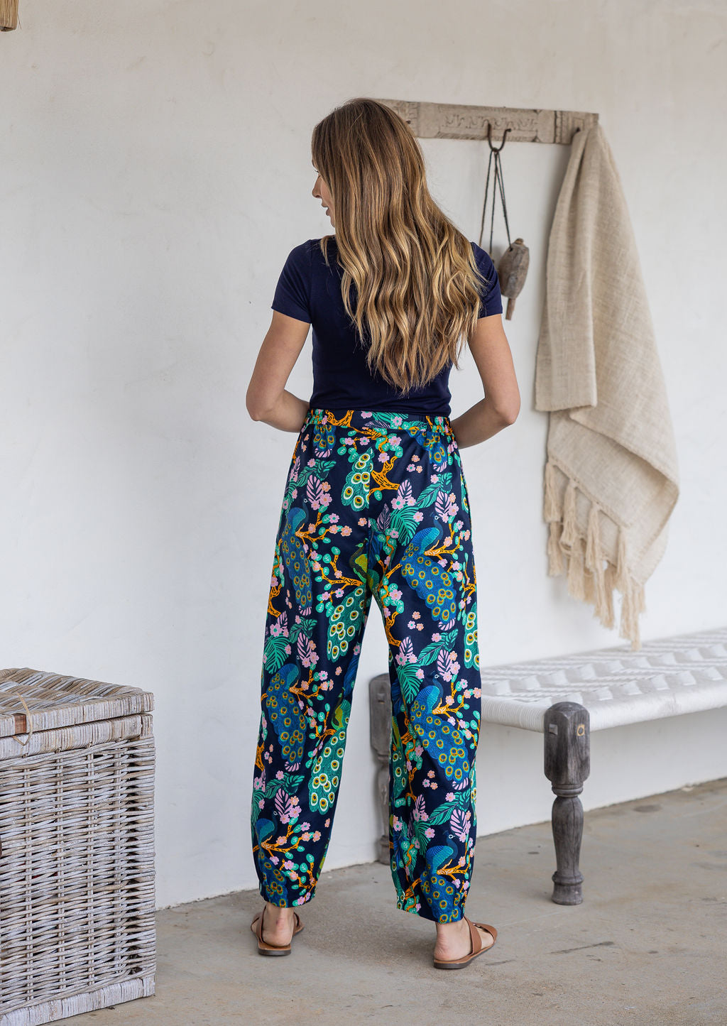 Woman stands backwards wearing a 100% cotton wide leg pants in navy based multicolour floral print with high waist elastic.