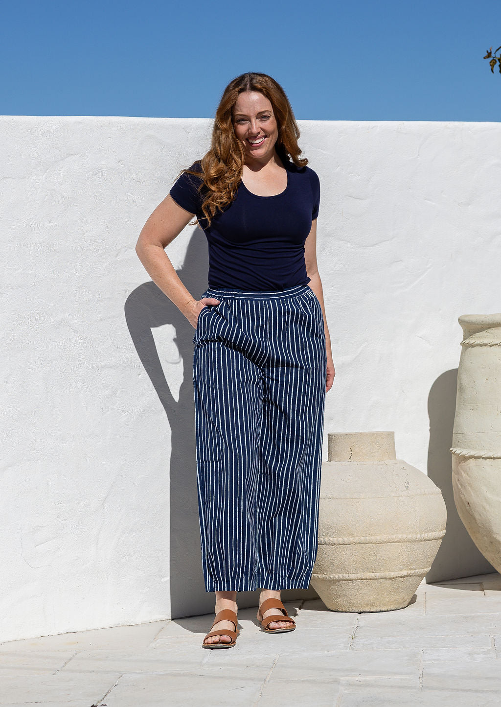 Woman wearing a 100% cotton wide leg pants in navy based white striped print with high waist elastic and one hand in pockets
