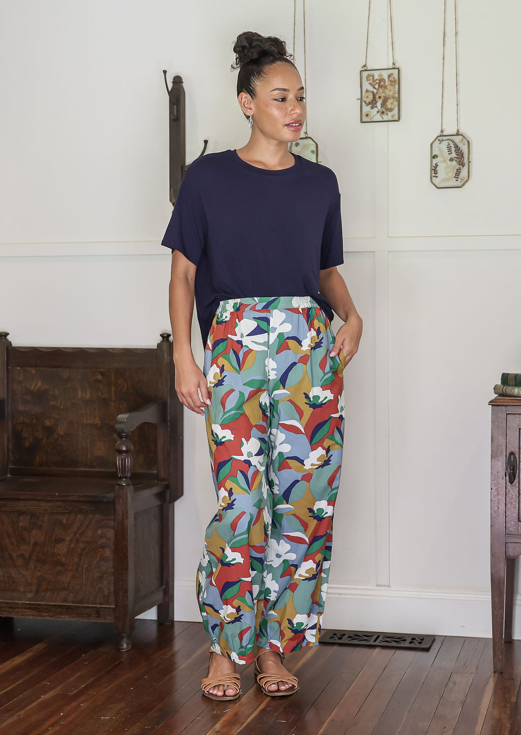 Woman wearing a navy top and colorful patterned pants in a room with wooden furniture.