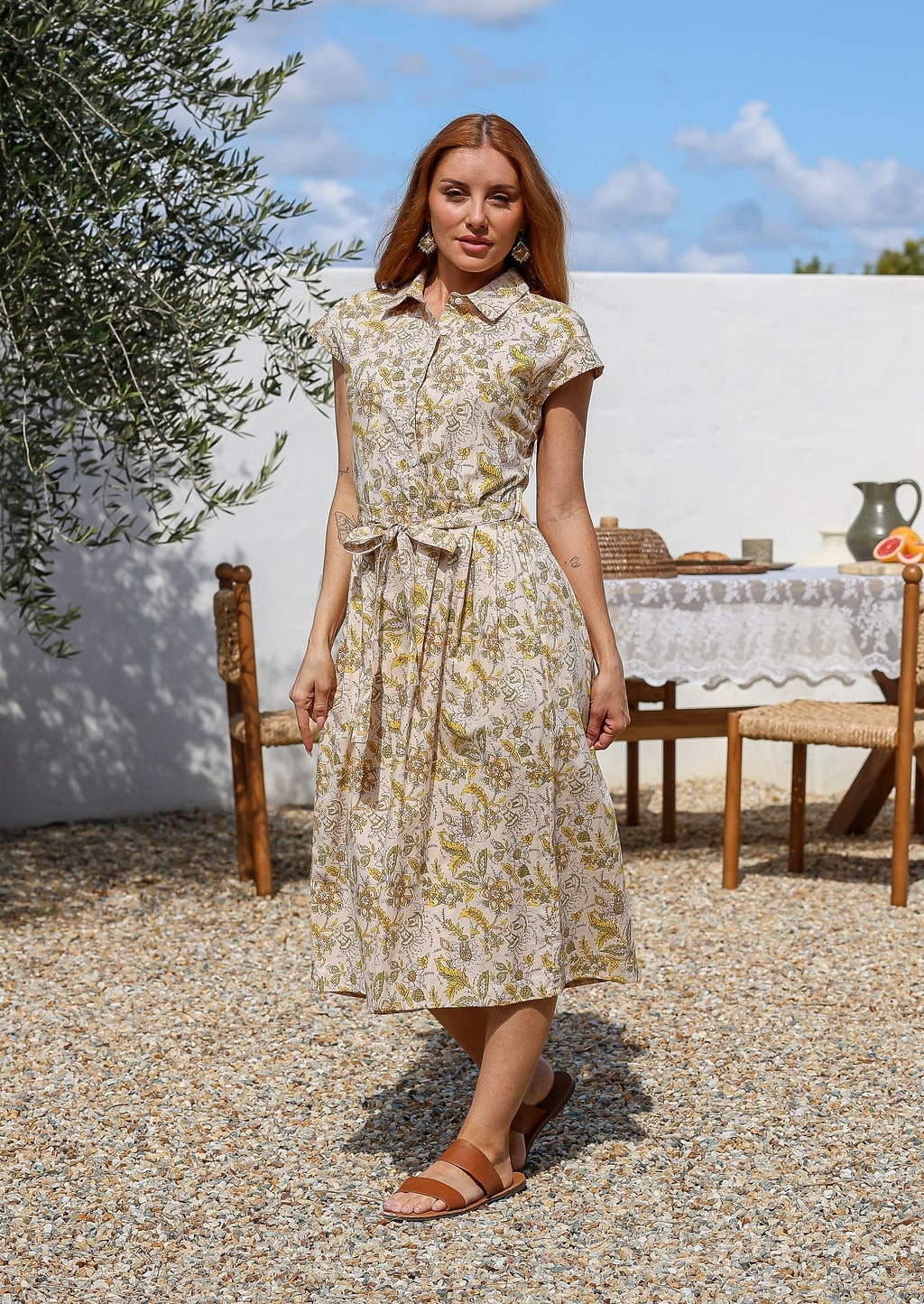 Woman wearing a midi length cream based floral cotton dress with buttoned bodice