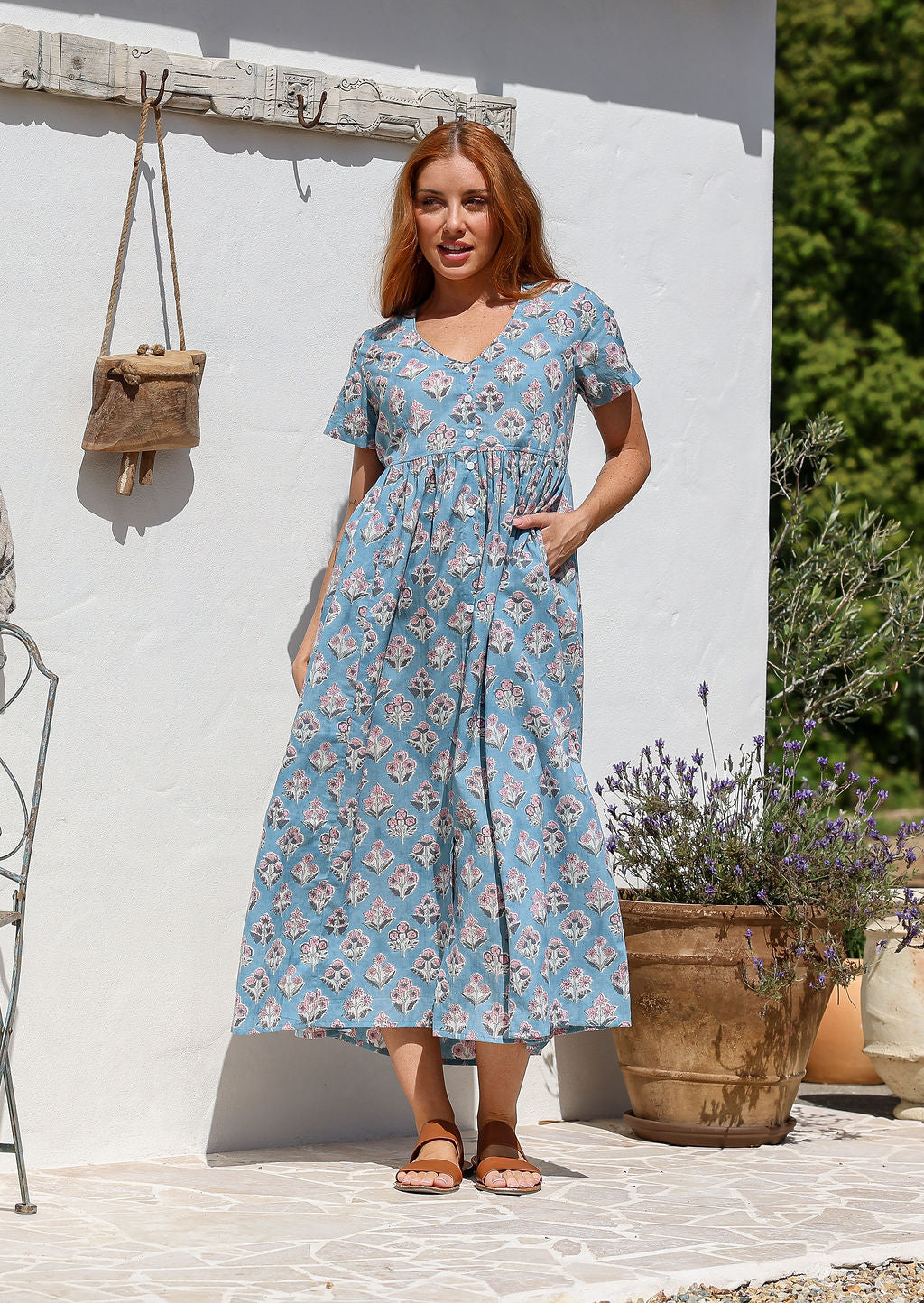 Woman standing in a 100% cotton floral print dress with a V-neckline, short sleeves, pockets, and buttons through to the knee.