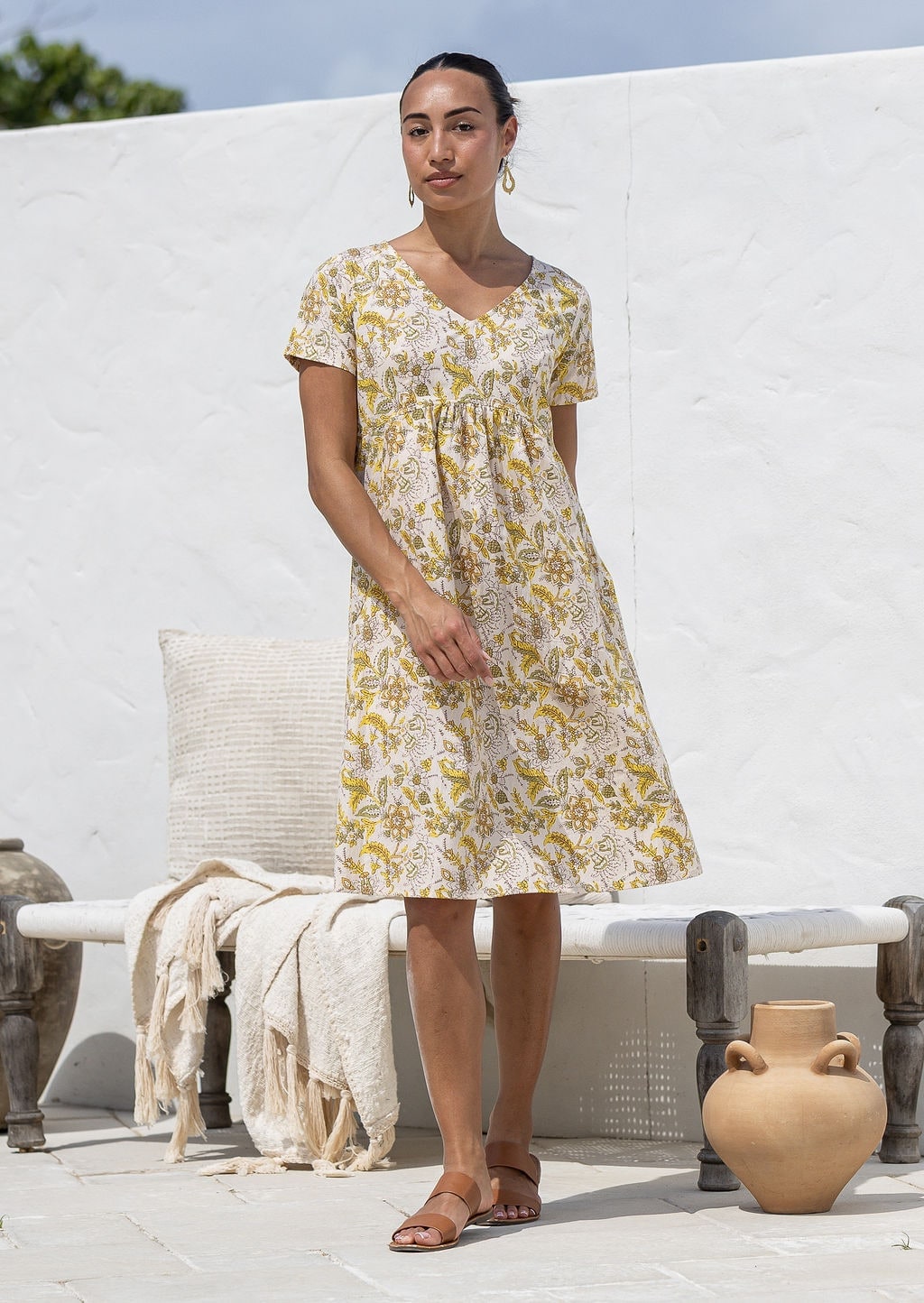 Woman wearing a cotton Etta Dress Primrose yellow floral print knee-length dress with V-neck.