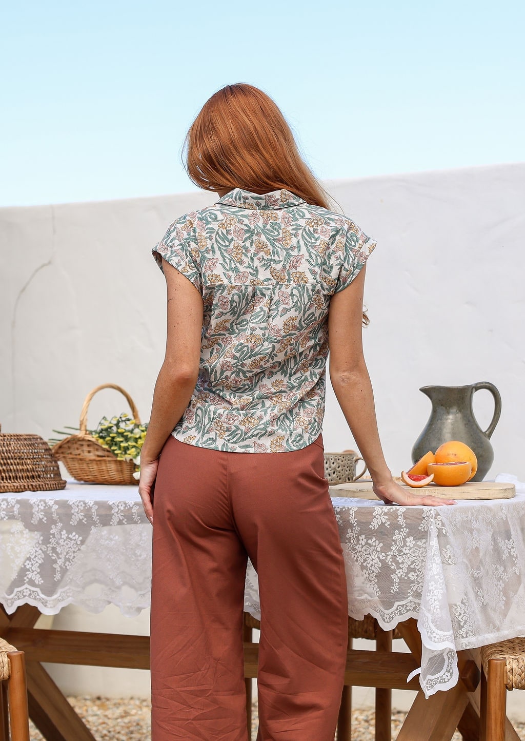 Woman standing backwards wearing slim fit cotton shirt in white based floral print with plain pants