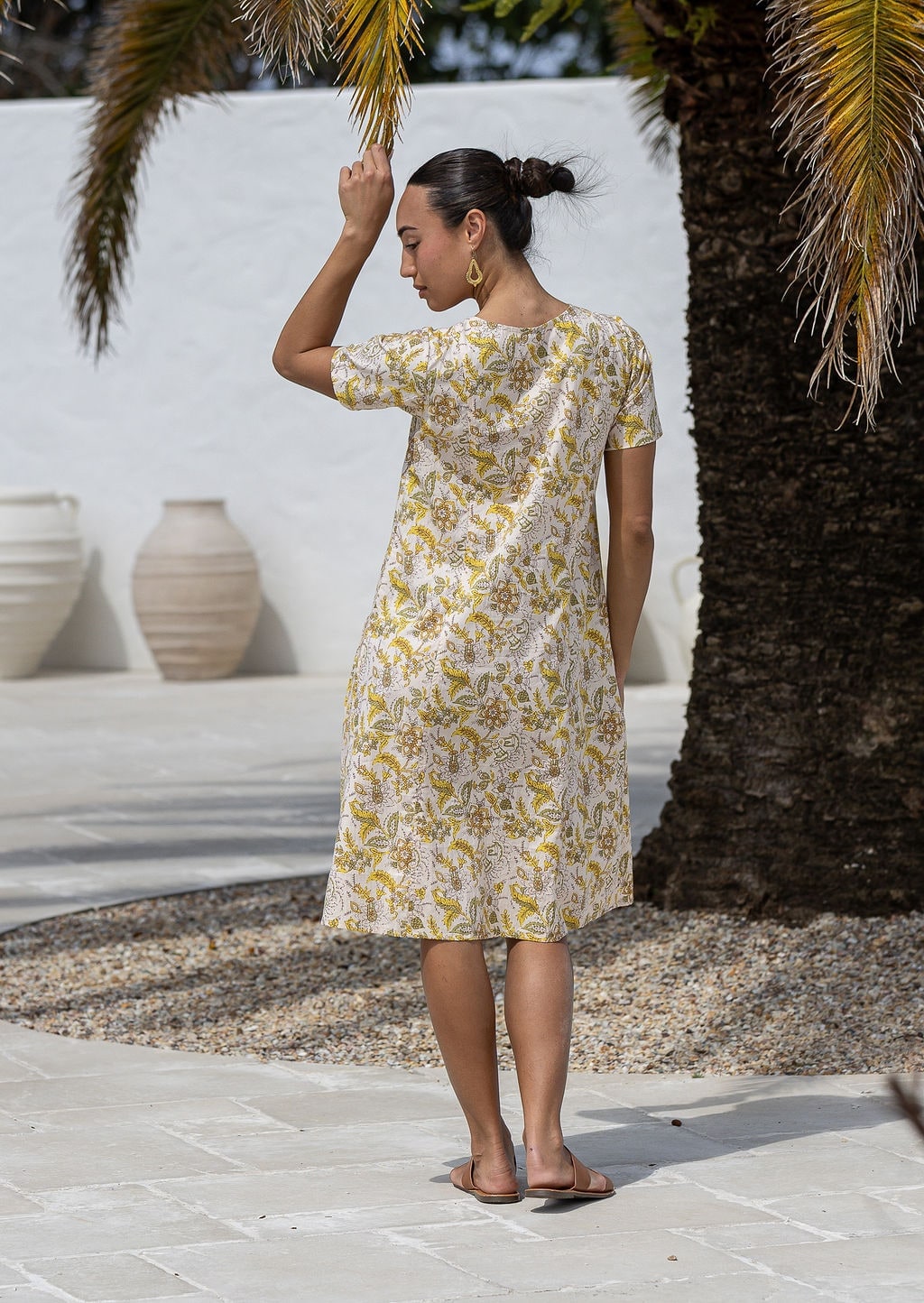 Woman stands backwards wearing a 100% cotton dress in cream based floral print with short sleeves.