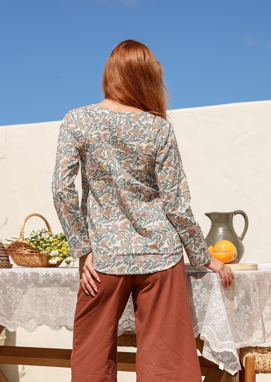 Long sleeve top in cream floral print with green and rust leaf pattern, back view on model outdoors.