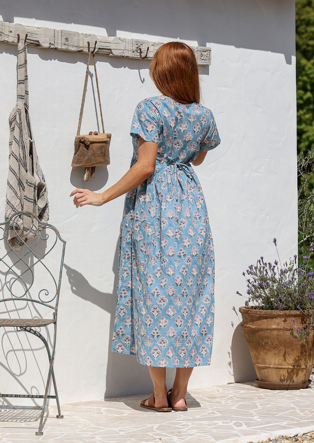 Woman stands backwards wearing a 100% cotton dress with short sleeves, pockets, and a drawstring tie at the back.