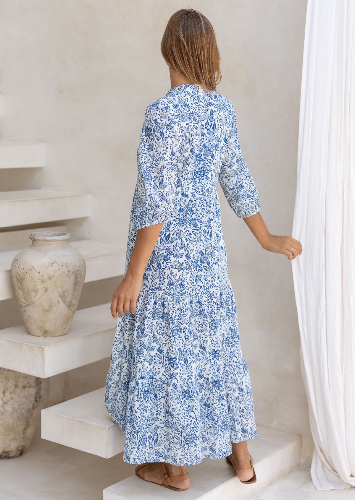 Model in 3/4 sleeves, relaxed fit tiered maxi dress in white based blue floral print.