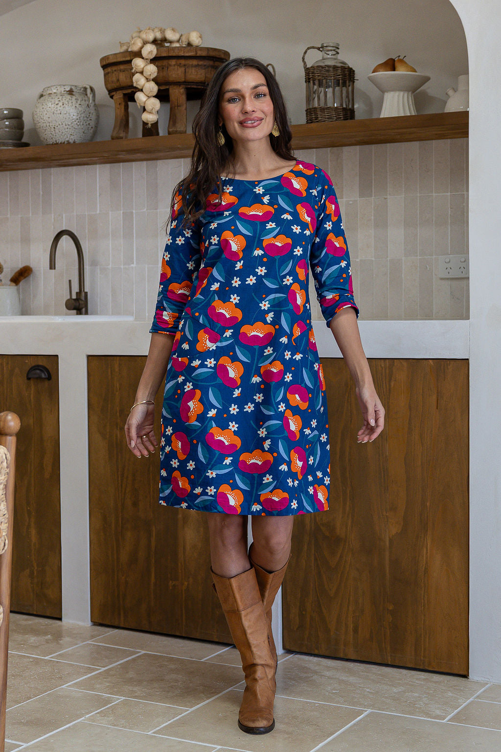 A woman wearing a 100% cotton knee-length dress in navy based floral print paired with brown boots.