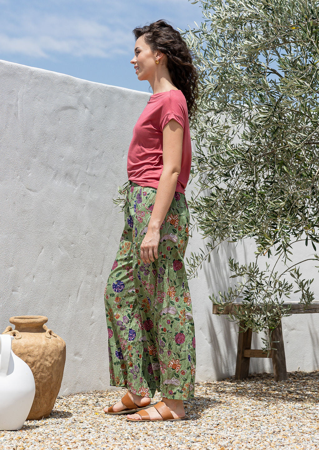 Side pose of model wearing wide leg, floral printed cotton pants with pockets and elastic waist at the back.