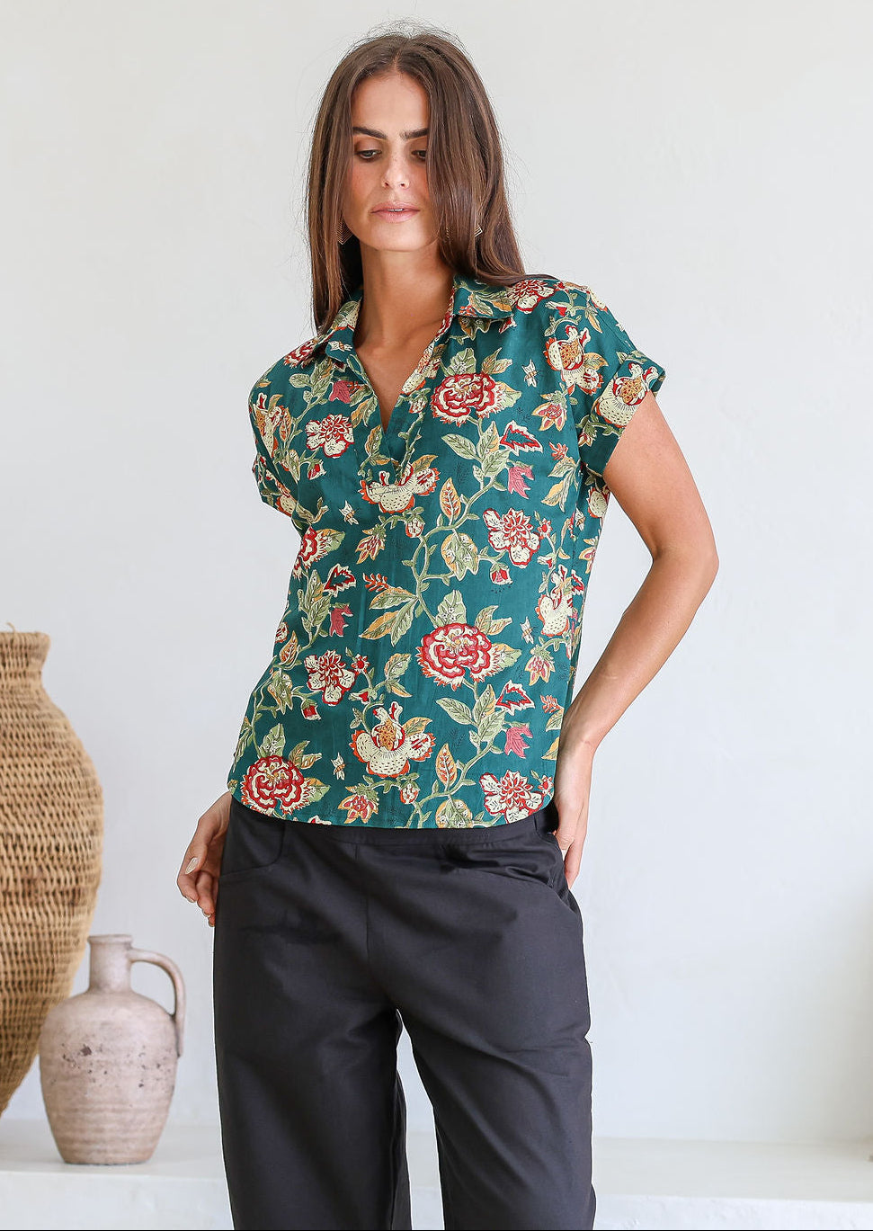 Woman wearing a green based relaxed fit, shirt style floral cotton top with black cotton pants.