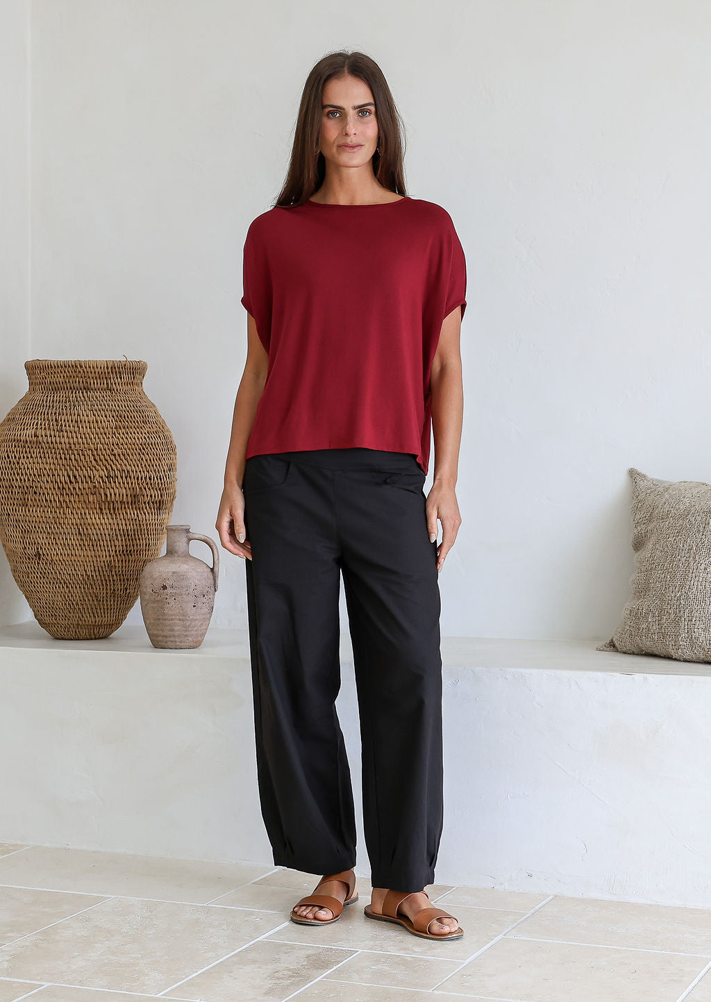Woman wearing a maroon soft stretch rayon batwing top and black pants in a minimalistic room.