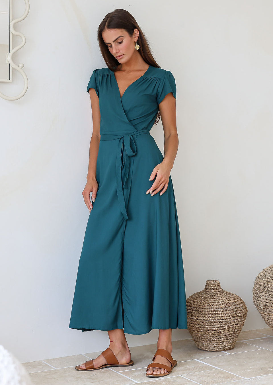 Woman leaning on a wall in a teal rayon wrap dress with gathers across front of shoulders