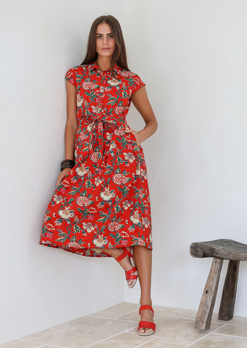 Woman wearing a shirt style cotton midi length dress with buttoned bodice, pockets, collar and cap sleeves