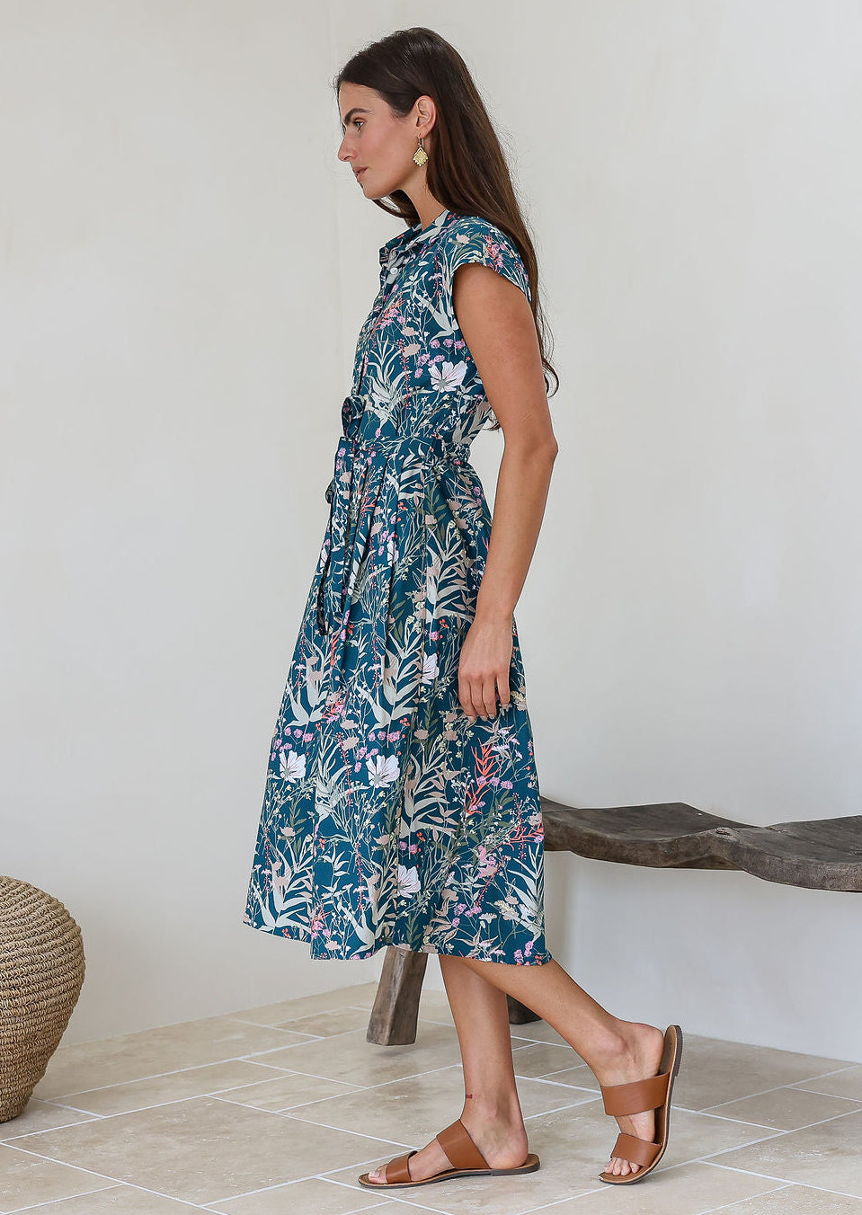 Model stands sideways wearing a shirt style cotton midi length dress with buttoned bodice, pockets, collar and cap sleeves