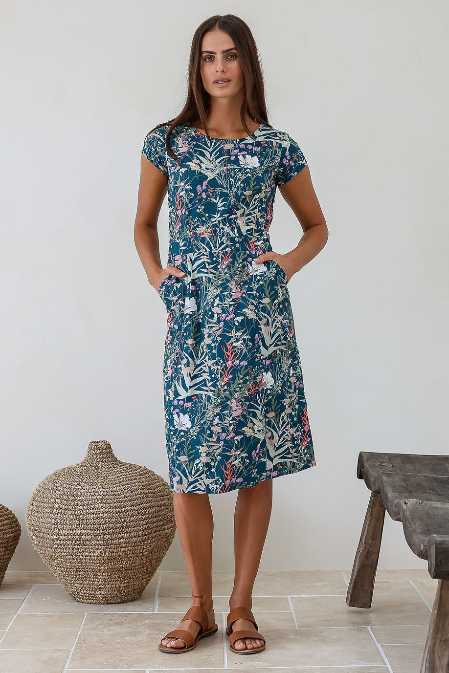 Model wears a simple knee length cotton dress with round neckline, short cap sleeves, pockets and a slight A-line skirt.