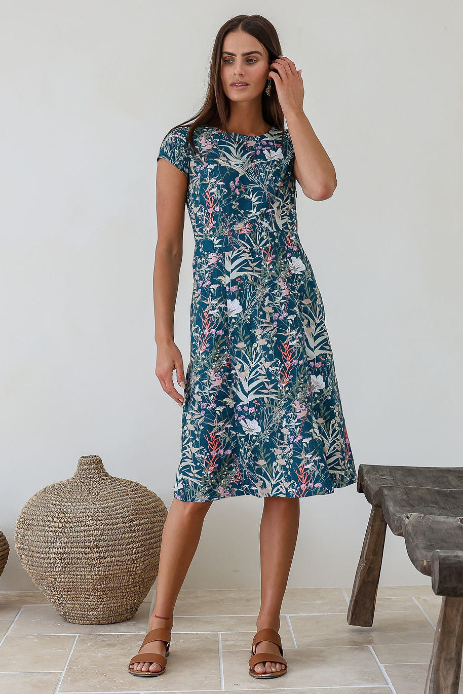 Model standing in a 100% cotton dress with of a beautiful teal based floral print dress.