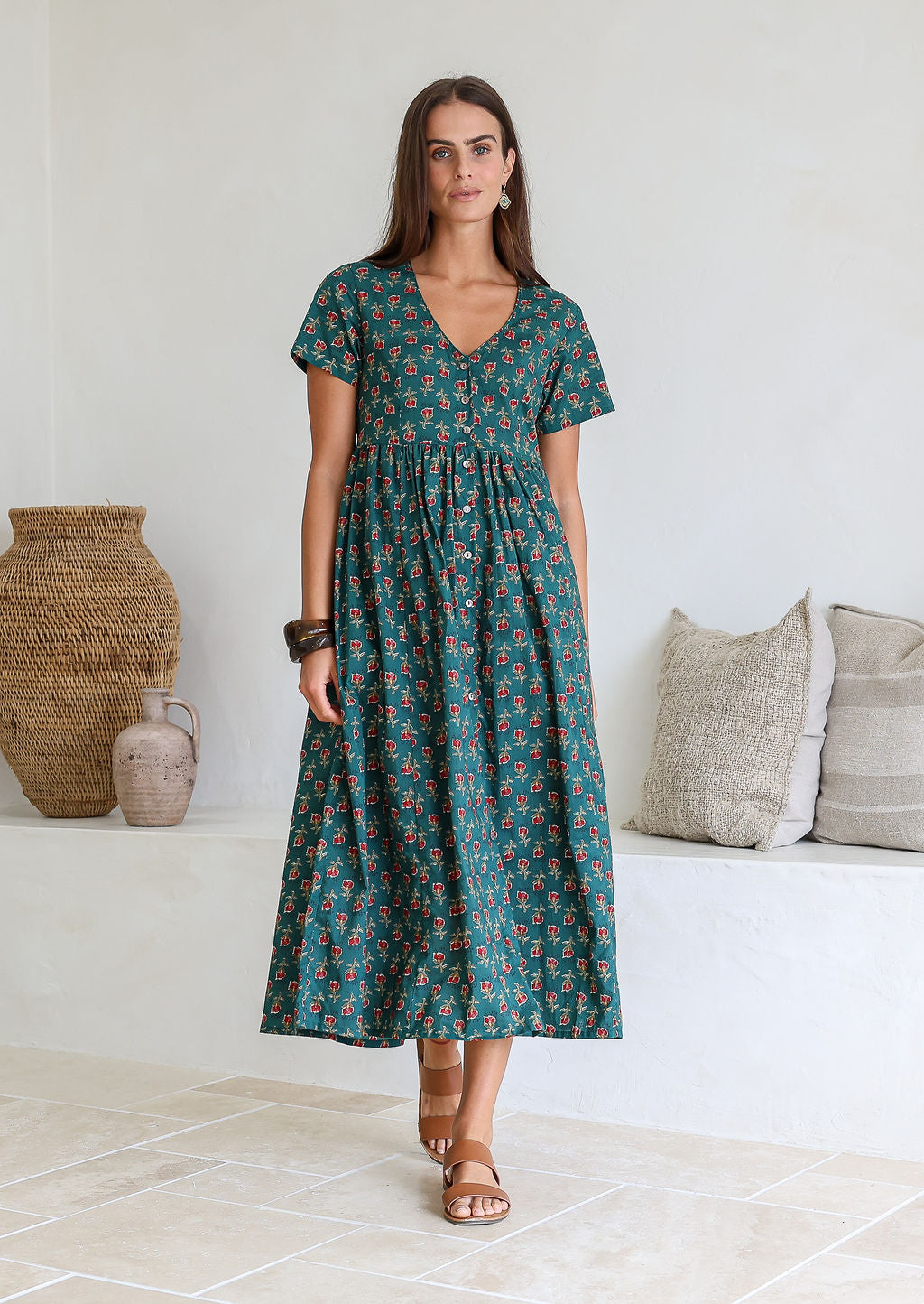 Woman wearing relaxed fit button through dress in bottle green based floral print with V neckline, pockets and short sleeves.