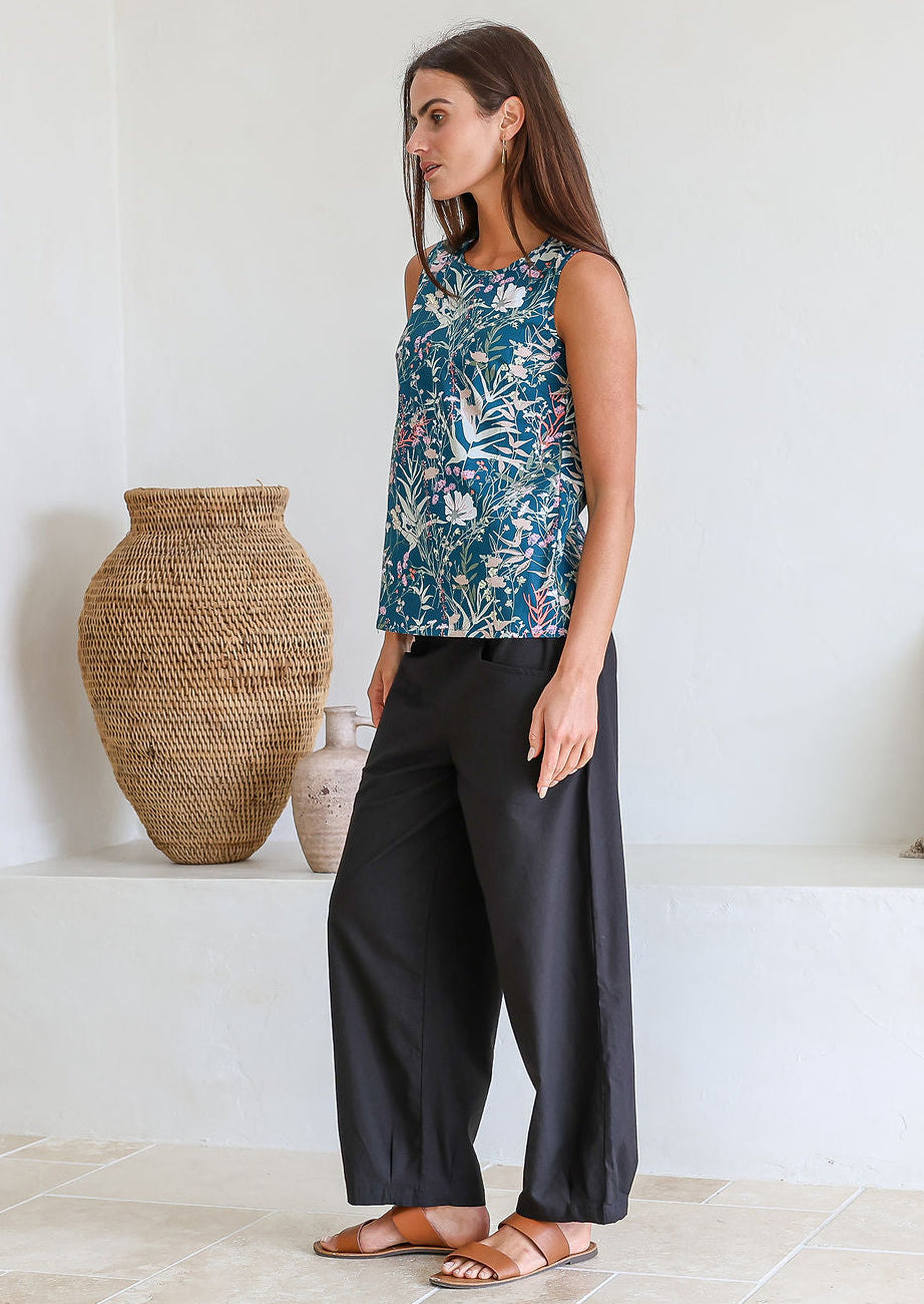 Woman standing sideways wearing a 100% cotton retro floral top, sleeveless design with side bust darts