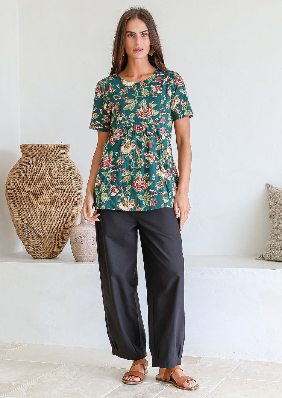 Woman wearing a bottle green based floral print top with short sleeves and an empire waistline, with deep pockets